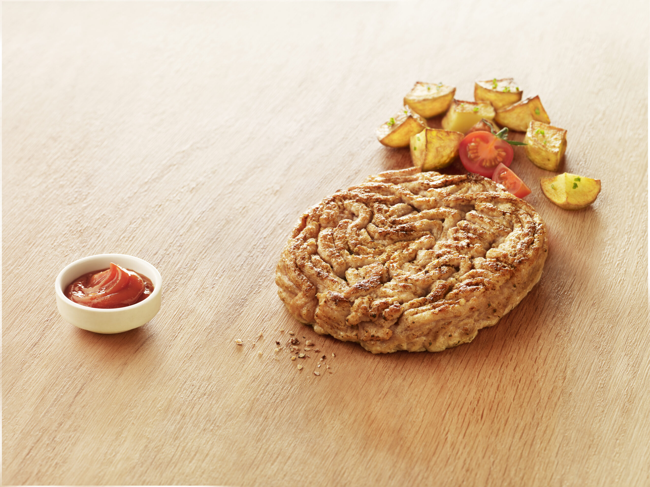 Haché de dinde Réghalal posé sur un fond bois avec des pommes de terre, des tomates cerises, des grains de poivre et un petit récipient de ketchup