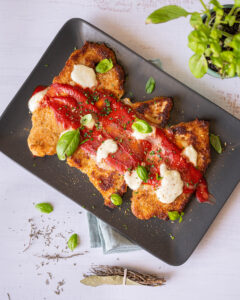 Escalopes de dinde à la Milanaise Réghalal dans une assiette noire, accompagnée de sauce tomate, mozzarella et feuilles de basilique.